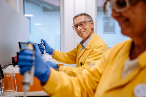 2 Kollegen in gelben Laborkitteln stehen beim Pippetieren