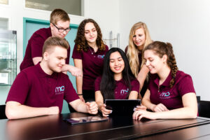 4 Azubis und eine Ausbilderin schauen sich zusammen etwas auf dem Ipad an